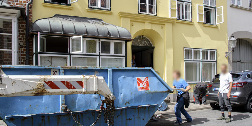 Vor einem Altbau füllen zwei Männer einen Bauschuttcontainer.