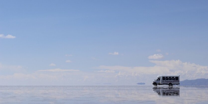 Blauer HImmel mit vereinzelten Wolken, unten sieht es aus, als ob ein Pick-Up auf einem See fahren würde