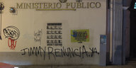 An einer Wand hängen verschiedene Plakate und ein Graffitispruch