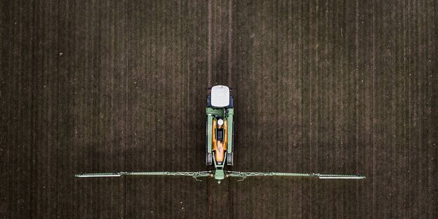 Ansicht von oben auf einen Traktor, der auf einem Feld Pestizide versprüht