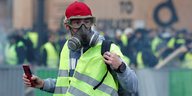 Ein Gelbwesten-Protestler mit Gasmaske und einem Smartphone in der Hand