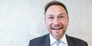 Christian Lindner, ein Mann in Anzug und Krawatte, lacht vor einer weißen Wand