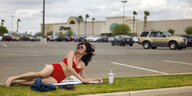 Eine Frau liegt im Bikini auf einem Grünstreifen auf dem Parkplatz eines Einkaufszentrums