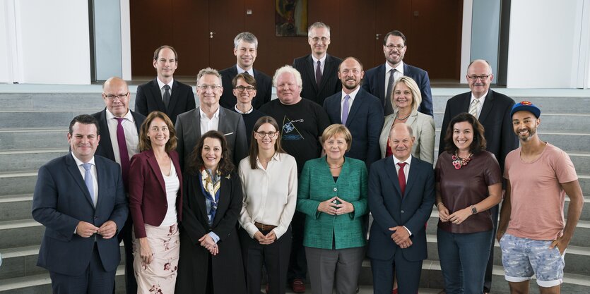 Menschen stehen nebeneinander und posieren für ein Foto, darunter Angela Merkel und Ijad Madisch, der ein Superman-Cap und kurze Hosen trägt