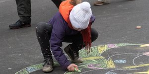 Ein Kind malt mitten auf der Friedrichstraße, die zwischen Tauben- und Kronenstraße für zwei Stunden gesperrt und in eine Fußgängerzone verwandelt wurde, mit Kreide auf dem Asphalt