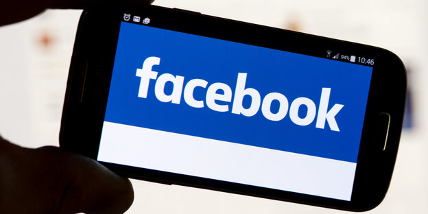 Facebook-Logo auf einem Smartphone, das von zwei Fingern gehalten wird