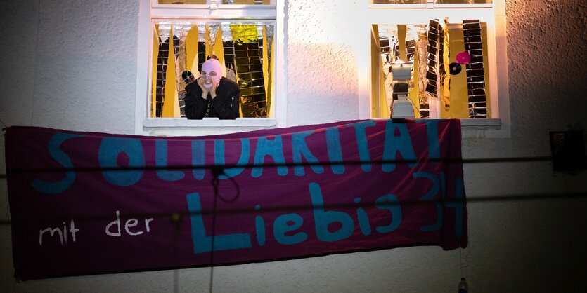 Eine vermummte Person schaut aus einem Fenster in der Liebigstraße 34