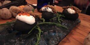 Ein sehr fancy angerichtetes Essen auf einer schwarzen Steinplatte, mit Algen garnier