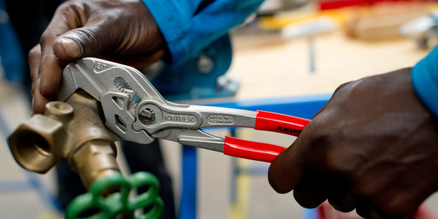 Die Hände eines schwarzen Mannes ziehen eine Schraube fest ildungszentrum der Siemens Professional Education an der Verdrahtung eines Schaltschranks