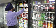 Ein Mann greift in einen mit Limonadenflaschen gefüllten Kühlschrank