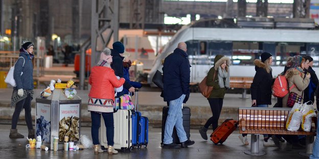Reisende in Winterkleidung stehen auf einem Bahnsteig