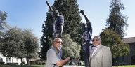 Tommie Smith und John Carlos stehen vor dem Denkmal, der sie in ihrer Pose mit ausgestreckter Faust bei der Siegerehrung zeigt