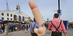Zwei männliche Oktoberfest-Besucher laufen mit einen aufgeblasenen Penis-Figur über das Gelände