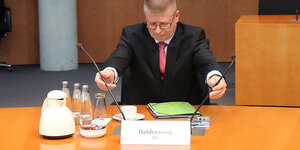 Verfassungsschutzchef Thomas Haldenwang sitzt an einem Tisch und richtet zwei Mikrofone