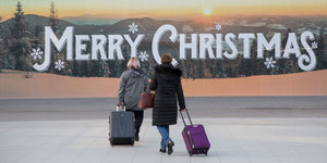 Reisende vor einem "Merry Christmas"-Schriftzug