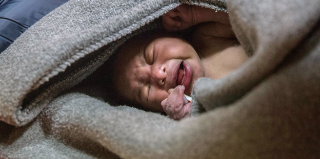 Ein schreiendes Baby liegt eingewickelt in eine Wolldecke