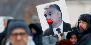 Ein Demonstrierender in Budapest, Ungarn, hält ein Plakat, auf dem Premierminister Viktor Orbáns Mund mit einer Weihnachtskugel gestopft ist
