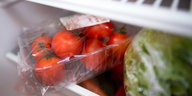 In Plastik verpackte Tomaten und Salatherzen liegen in einem Kühlschrank.