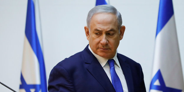 Israels Ministerpräsident Benjamin Netanjahu steht vor israelischen Fahnen