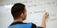 Ein junger Mann übt an einer Tafel das Schreiben in deutscher Sprache.