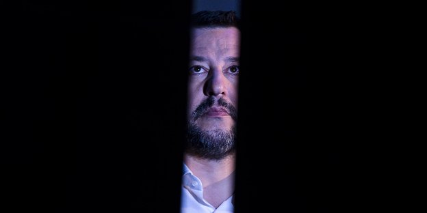 Salvini guckt durch einen schmalen Spalt in breitem Schwarz