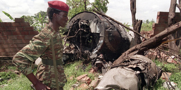 Mann in Tarnuniform und mit rotem Barrett vor einem Flugzeugwrack