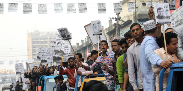 ganz viele Menschen auf der Straße, ihre Hände halten Stöcke mit Plakaten in die Höhe. Auf den Plakaten: Politikerkonterfeis