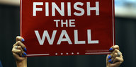 Eine Person hält ein Schild hoch, auf dem "Finish the Wall" steht