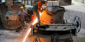 Arbeiter in einer Gießerei gießen glühenden Stahl aus einer großen Wanne