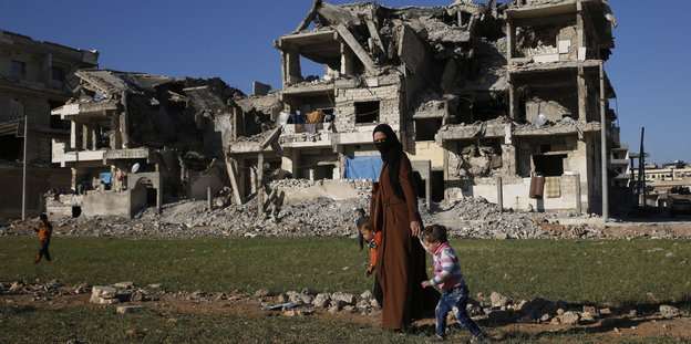 Eine Syrerin mit ihren Kindern zwischen vom Krieg zerstörten Häusern