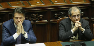 Giuseppe Conte und Giovanni Tria sitzen nebeneinander und halten sich die Hände vors Gesicht
