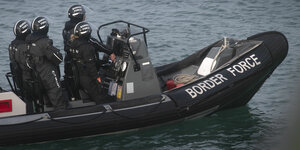 Vier Menschen in schwarzen Anzügen und Helmen auf einem schwarzen Schlauchboot auf offenem Meer