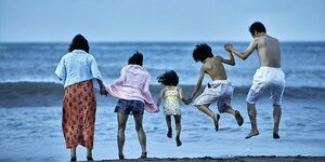 Drei Erwachsene und zwei Kinder fassen sich am Strand bei den Händen.