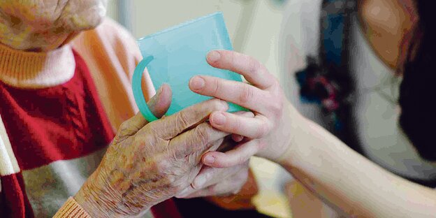 Eine Pflegerin reicht einem alten Menschen einen Becher.