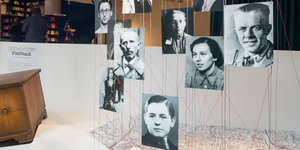 Historische Portraitfotos hängen von der Decke und sind mit Fäden mit einem Stadtplan verbunden.