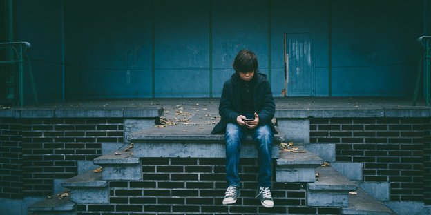 Ein Junge sitzt auf steinernen Stufen und guckt auf sein Handy