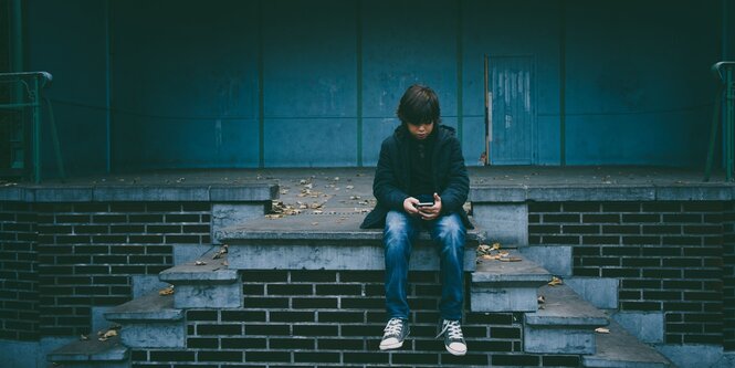 Ein Junge sitzt auf steinernen Stufen und guckt auf sein Handy