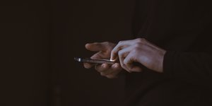 Hände berühren ein Iphone vor schwarzem Hintergrund