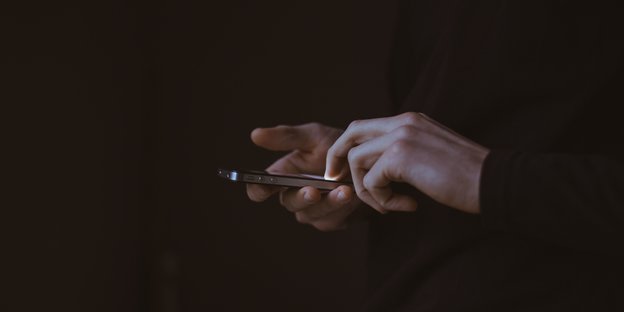 Hände berühren ein Iphone vor schwarzem Hintergrund