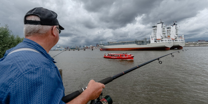 Ein Mann angelt in Hamburg an der Norderelbe gegenüber der Hafencity.