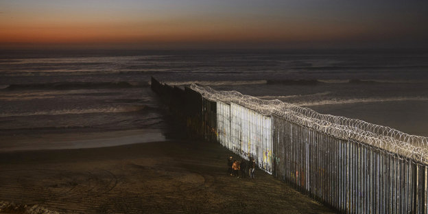 Menschen stehen an der Grenzmauer zwischen Mexiko und San Diego, Kalifornien, als die Sonne in Playas de Tijuana über dem Strand untergeht