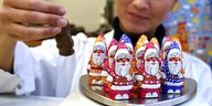 Eine Frau nimmt einen von mehreren Weihnachtsmännern aus Schokolade in die Hand.