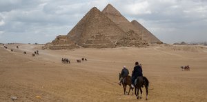 Die Pyramiden in Gizeh, davor Reiter auf Kamelen