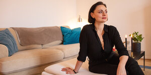 Eine Frau sitzt auf einem Hocker in ihrem Wohnzimmer