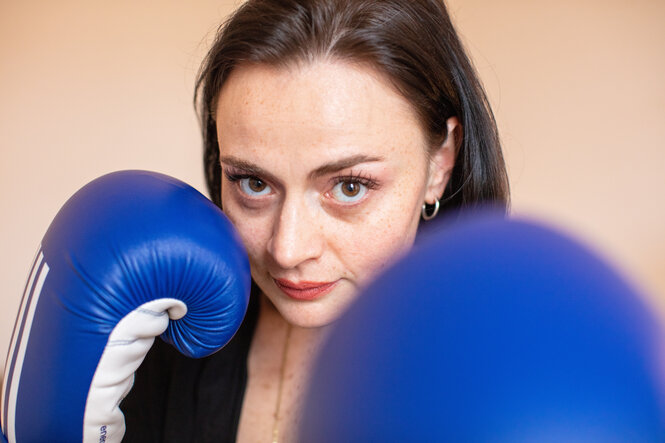 Eine Frau trägt blaue Boxhandschuhe und schaut in die Kamera