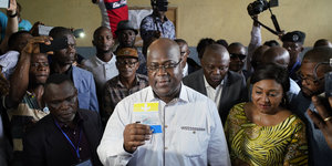Ein Mann hält einen Stimmzettel in die Kamera, daneben stehen viele Personen