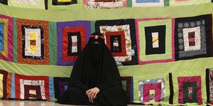 Eine vollverschleierte Frau sitzt vor einem Wandschmuck