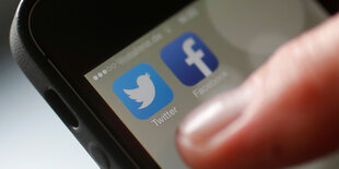 Ein Finger auf einem Smartphone, dessen Bildschirm die Apps von Twitter und Facebook zeigt