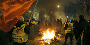 DemonstrantInnen mit gelben Westen stehen neben einem brennenden Fahrrad auf der Avenue des Champs-Elysée