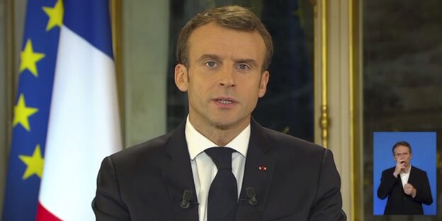 Macron auf einem Fernsehbildschirm steht vor einer europäischen und französischen Flagge. Unten rechts wird seine Rede auf Gebärdensprache übersetzt Macron auf einem Fernsehbildschirm steht vor einer europäischen und französischen Flagge. Unten rechts wird seine Rede auf Gebärdensprache übersetzt